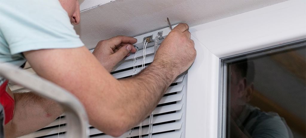 Person adjusting stuck window blind headrail with screwdriver for repair maintenance