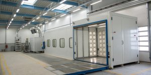 Industrial paint booth with both a large metal structure and smaller components inside, demonstrating its capacity to handle parts of different sizes.