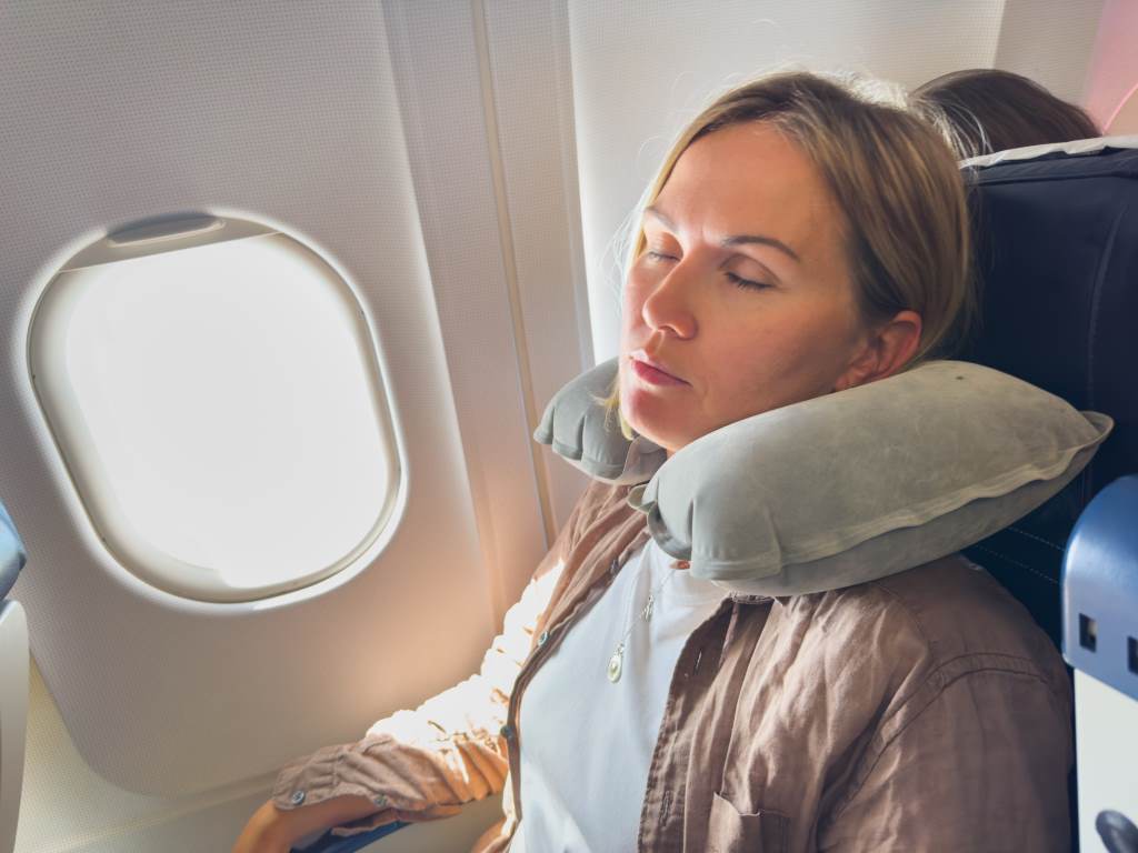 Woman sleeping peacefully on plane with twisted Dot&Dot travel pillow supporting neck