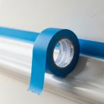 A roll of blue painter's tape applied neatly along white wall trim before painting.
